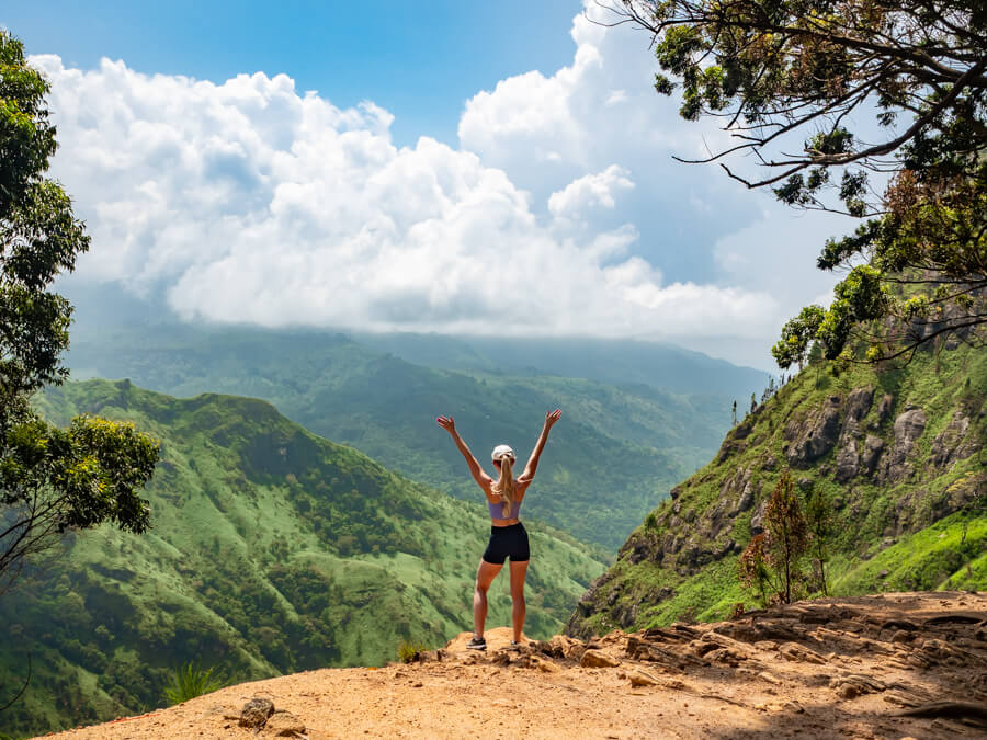 Hiker standing on a mountain summit viewpoint overlooking the green valley of Ella